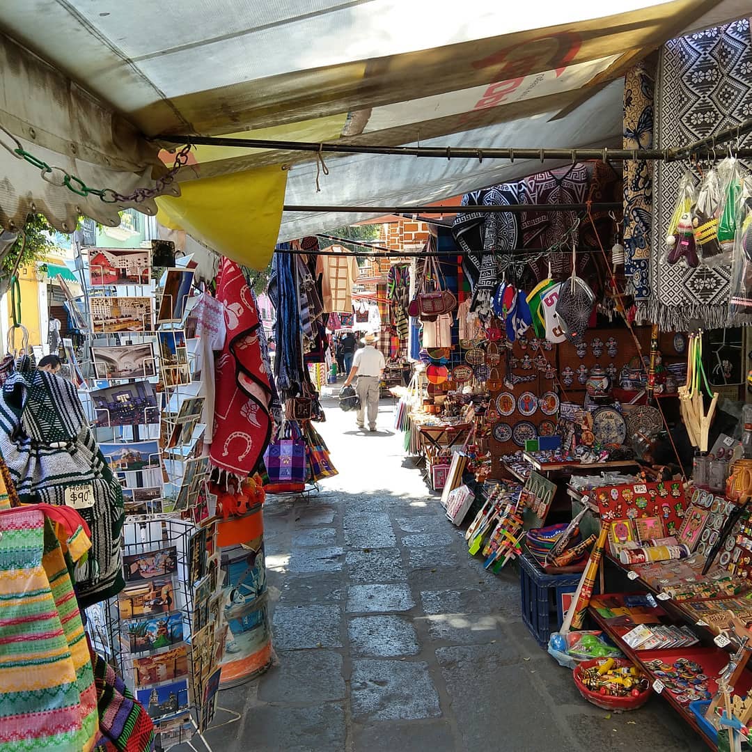 Narrow path of market stalls selling postcards, bags, plates, and touristy souvenirs