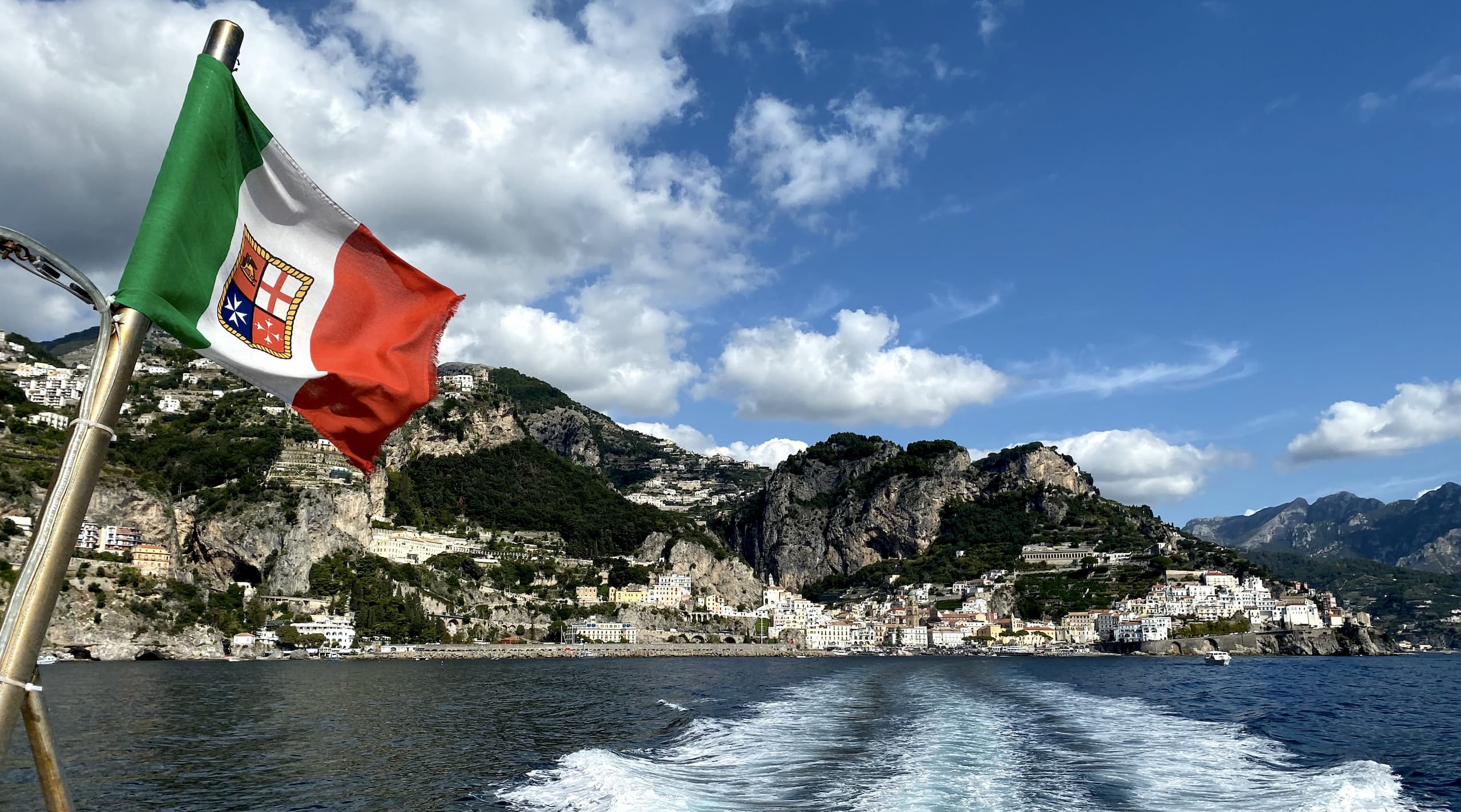 Italian flag waving on the end of a boat with coastline in background.