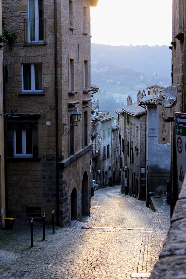 Buildings along a narrow, windy, descending, cobblestone street.