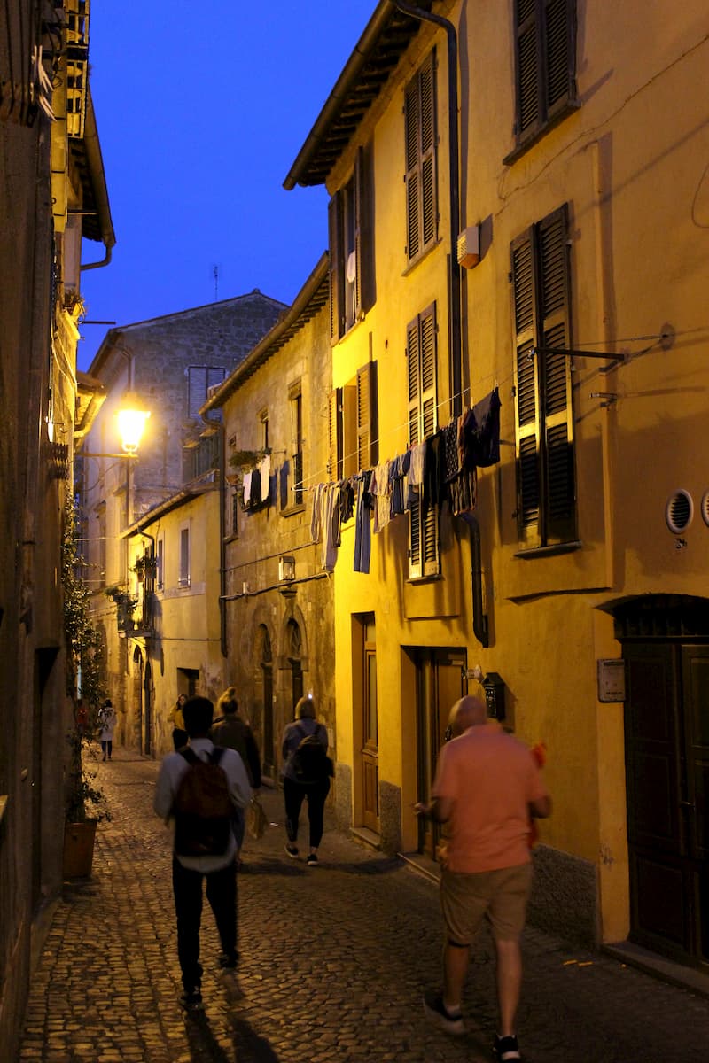 people walking down a cobblestone alleyway at night