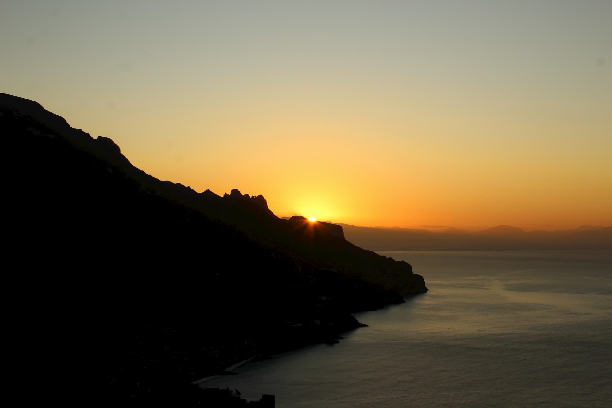 Silhouette of a coastal hillside with the sun peeking over a ridge