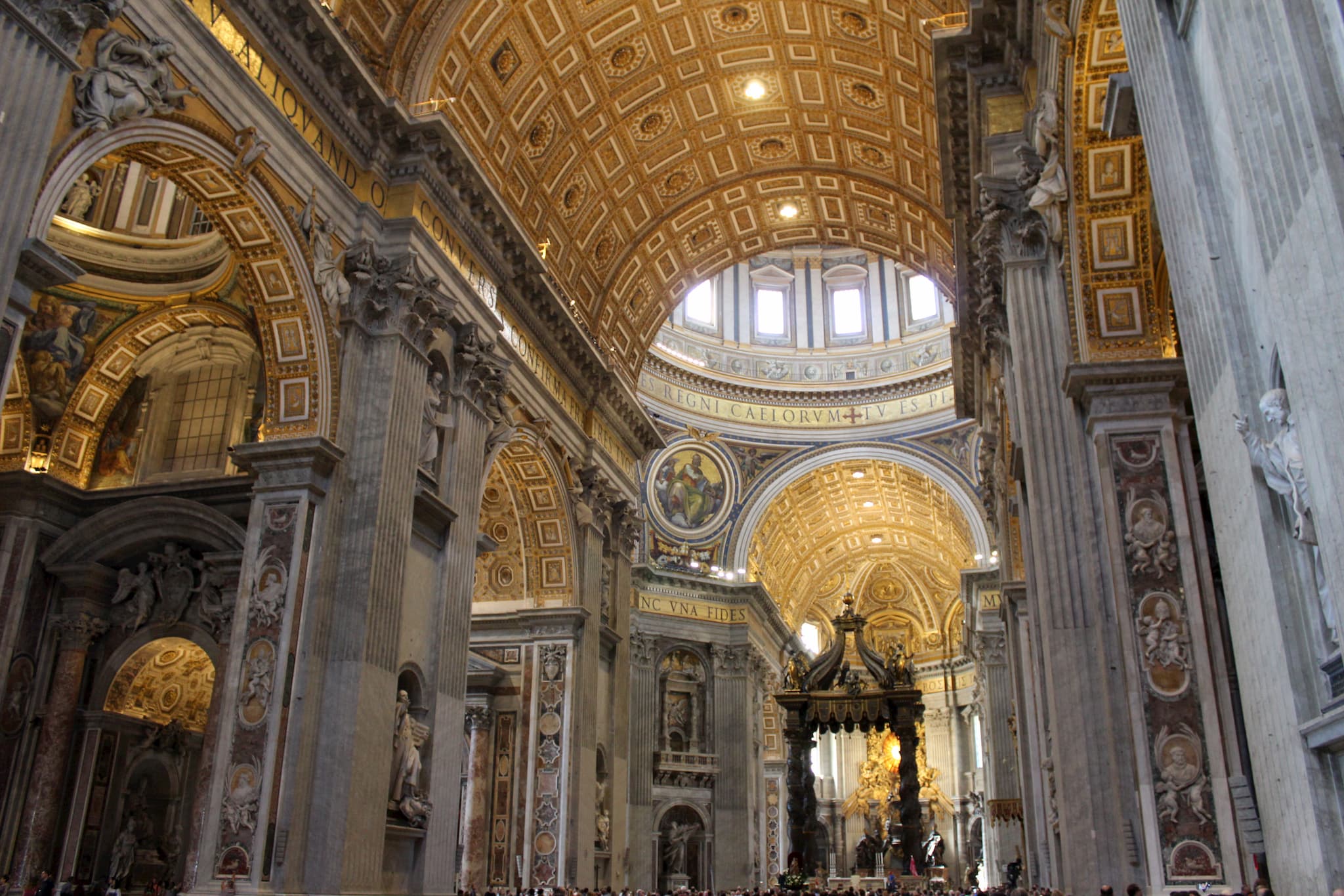 Inside of massive stone church with gold accents on arched roof and a windowed dome over a black platform