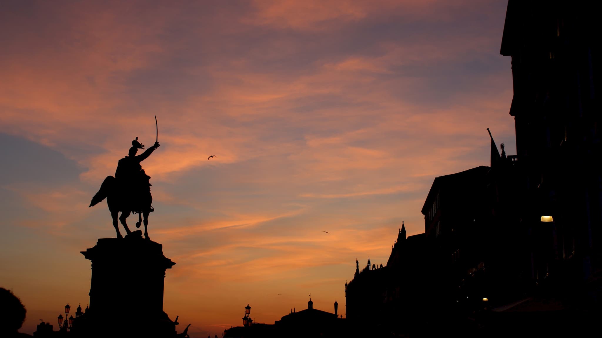 Silhouette of statue with orange clouds in the sky at sunset.