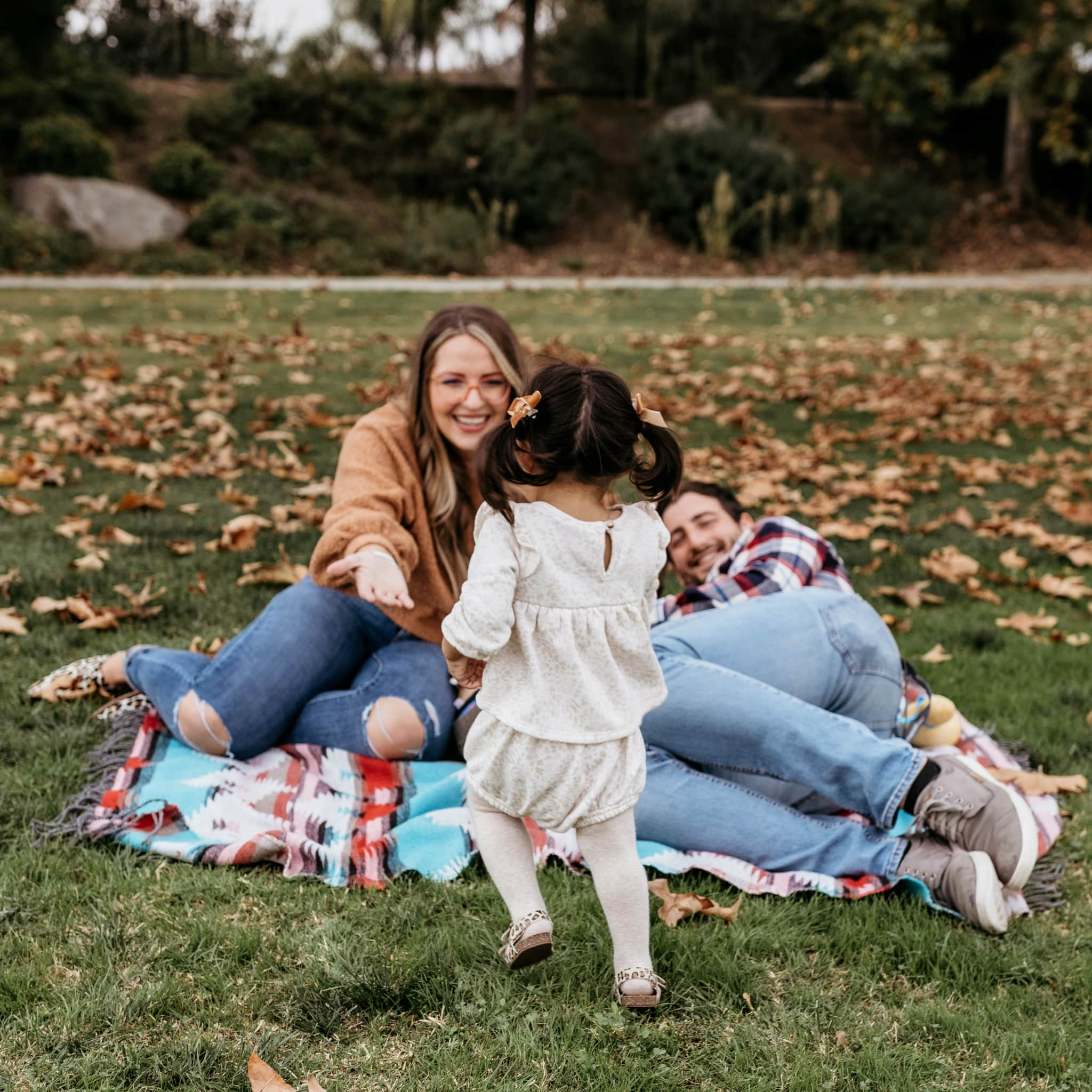 small girl running to woman with open arm on picnic blanket.