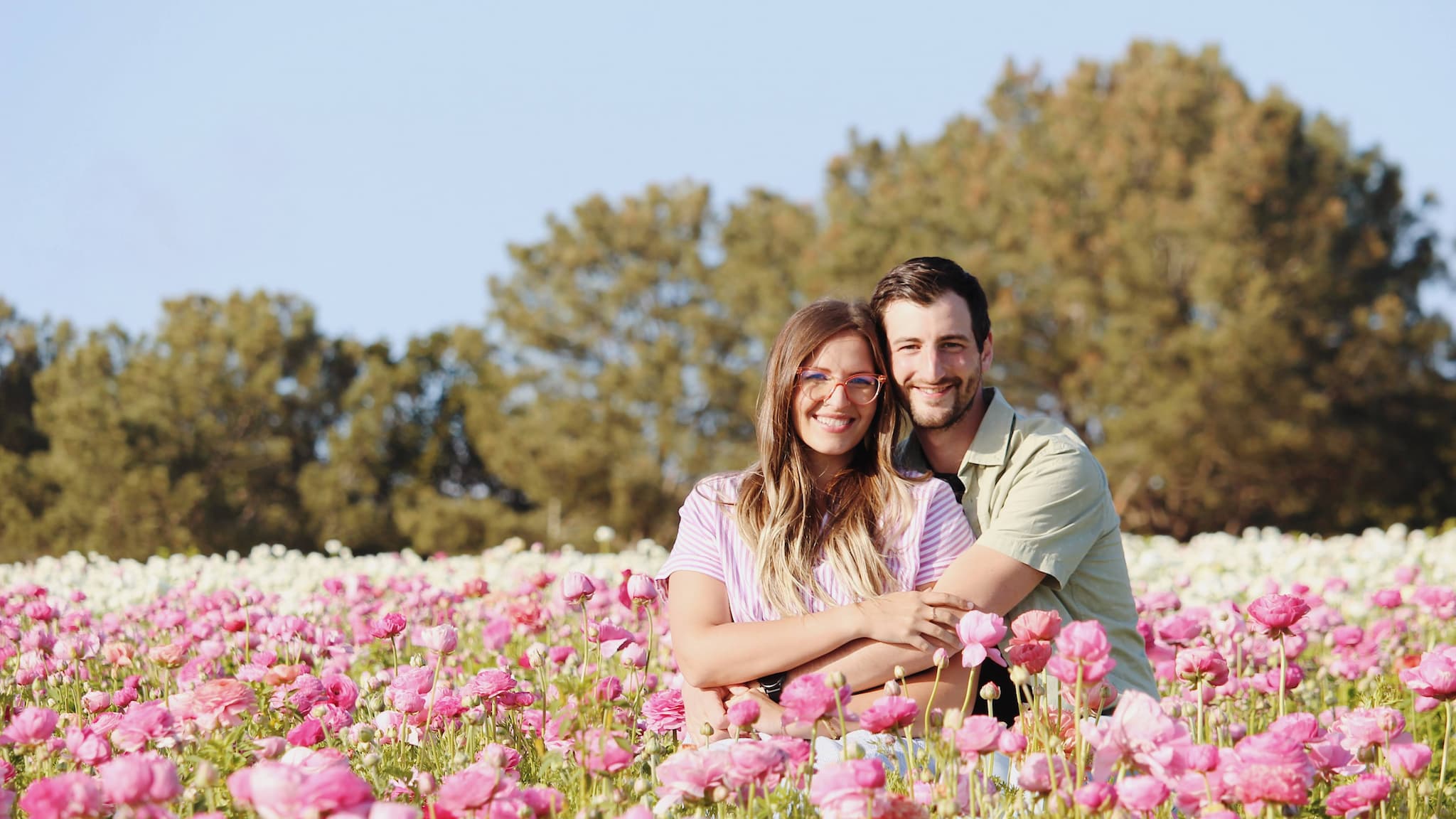 Couple sitting in flower field smiling at camera.