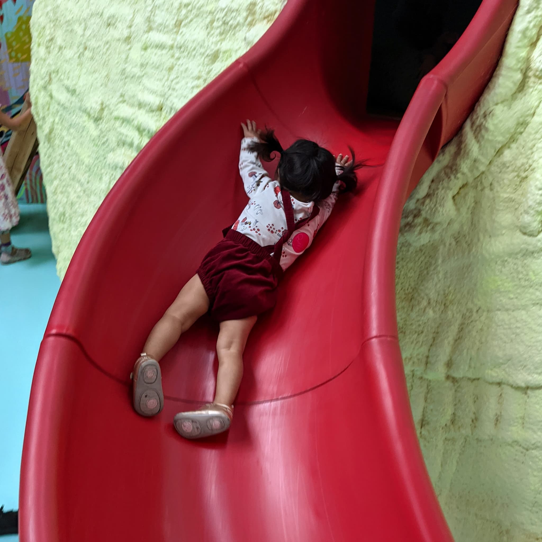 Baby girl sliding down a slide on her belly.