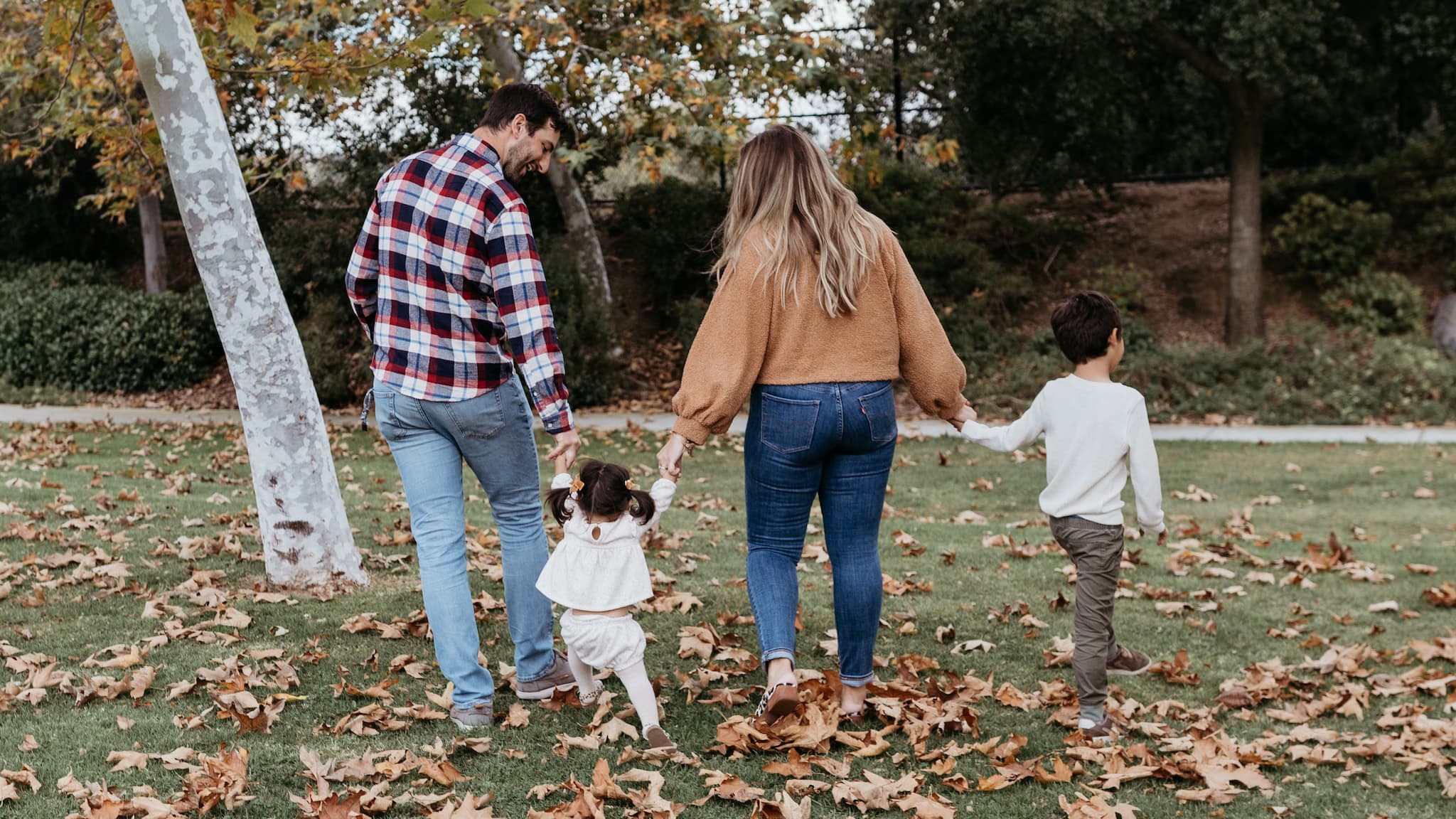 two adults walking with two kids in fall leaves.