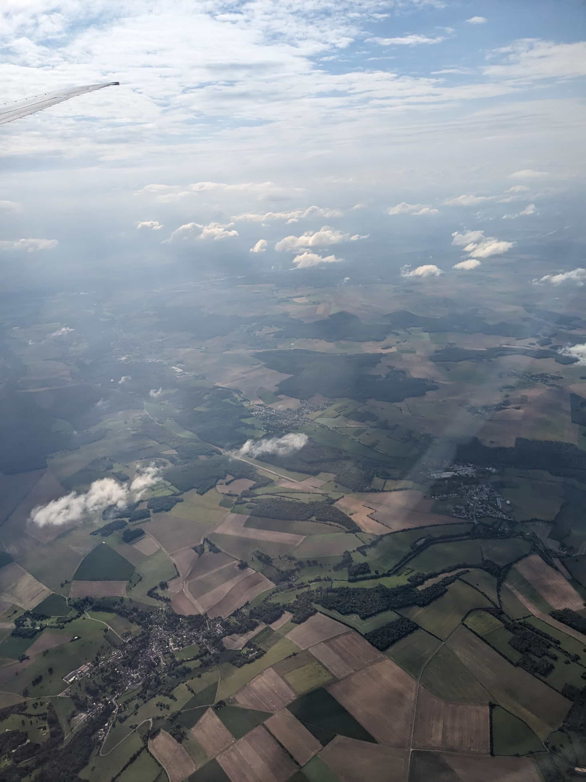 Looking down on small clouds and farmland. A plane wingtip is visible in the corner of the picture.