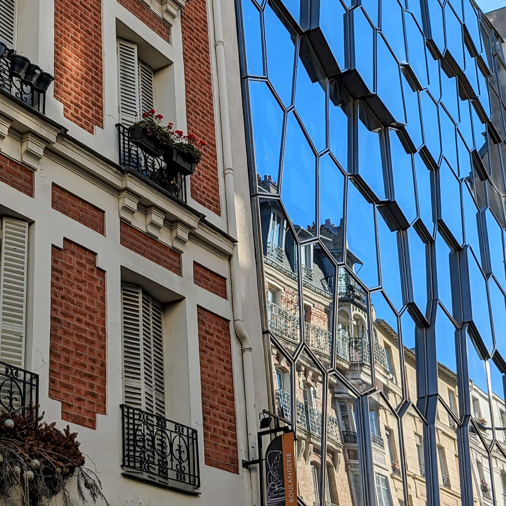 Brick building next to a glass faced building showing another brick building in its reflection.