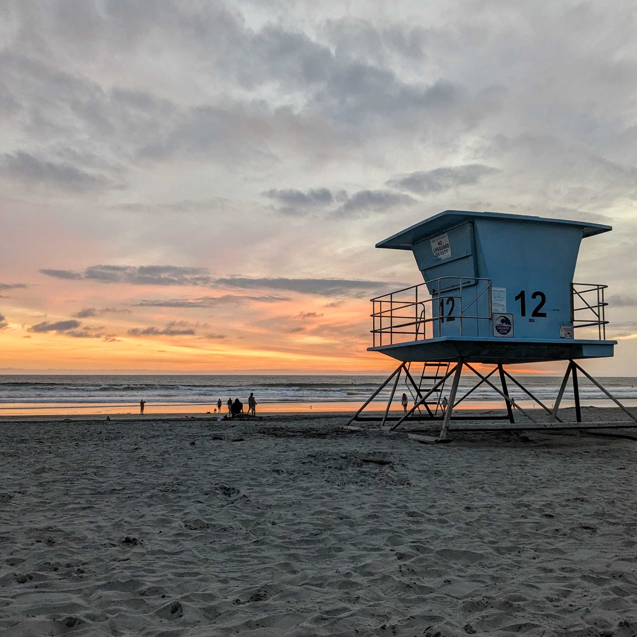 Looking out from a beach at a colorful sunset with a lifeguard tower in the foreground.