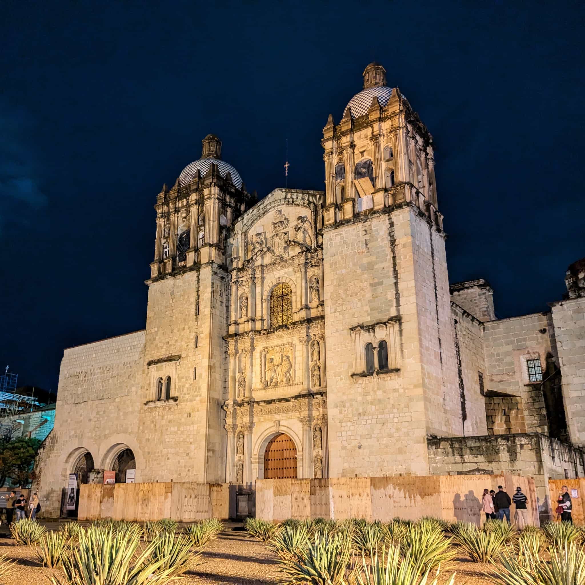 Large tan stone church against a deep blue night sky with agave planted in front.