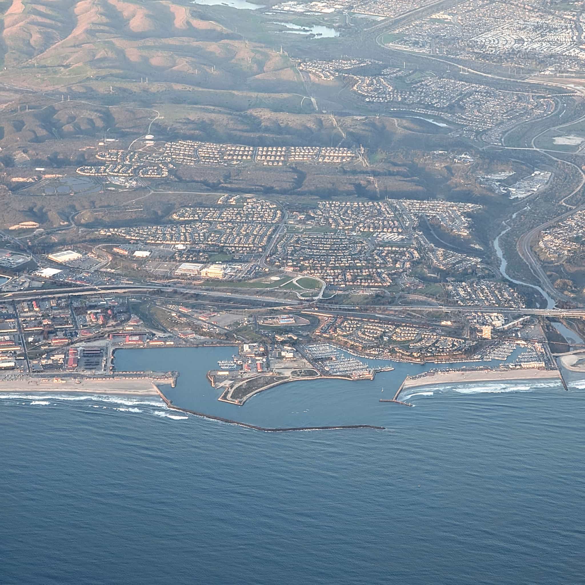 areal photo of a coastline showing waves breaking outside of a big harbor