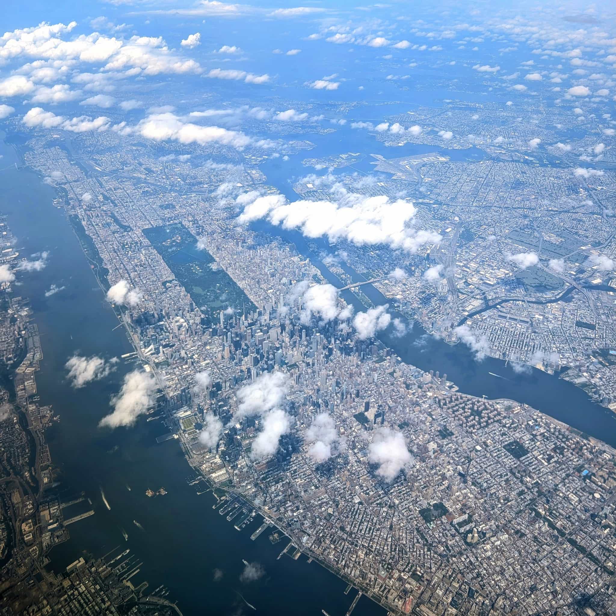 View from an airplane with all of Manhattan visible through scattered clouds. Central Park and the sky scrapers of midtown stand out.