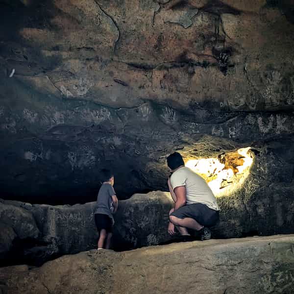 A man and boy looking at a grafitied, stone cliff face with a flashlight.
