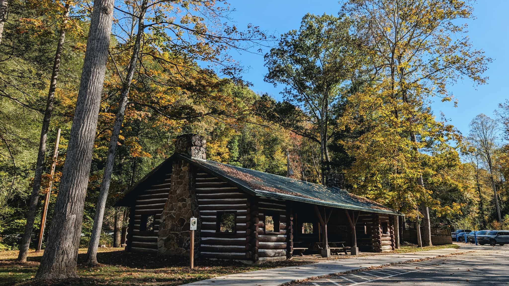 A picnic shelter built with logs surrounded by trees with autumn leaves.
