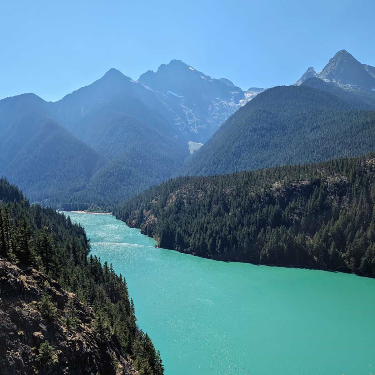 Multiple mountain peaks rising up behind a light blue lake.