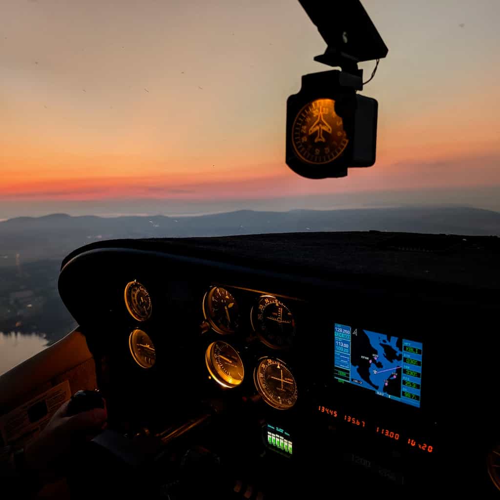The instrument panel of a small plane with an sky in various shades of orange in the background.