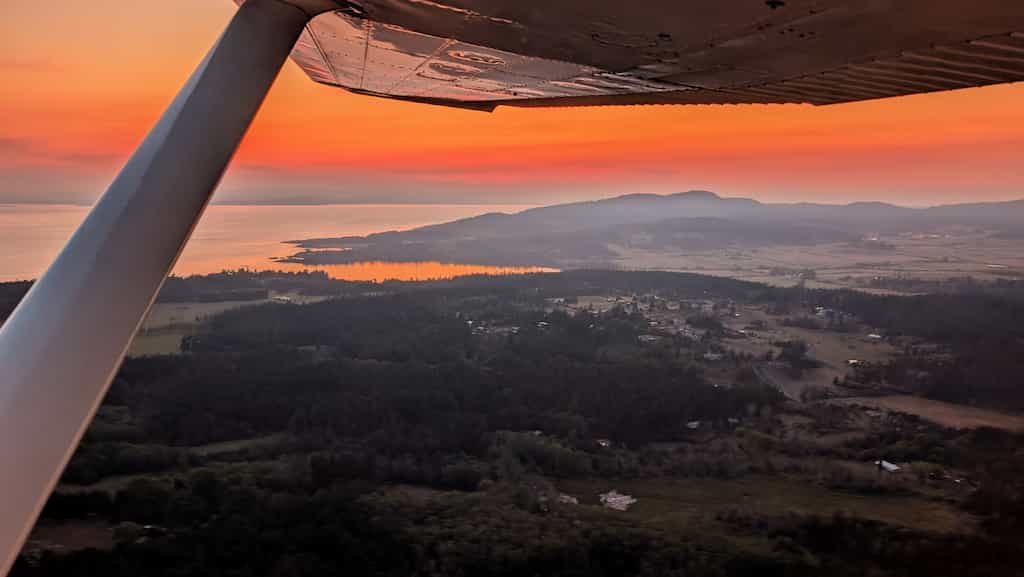Looking out the side of a small plane at a orange sunset over an island.