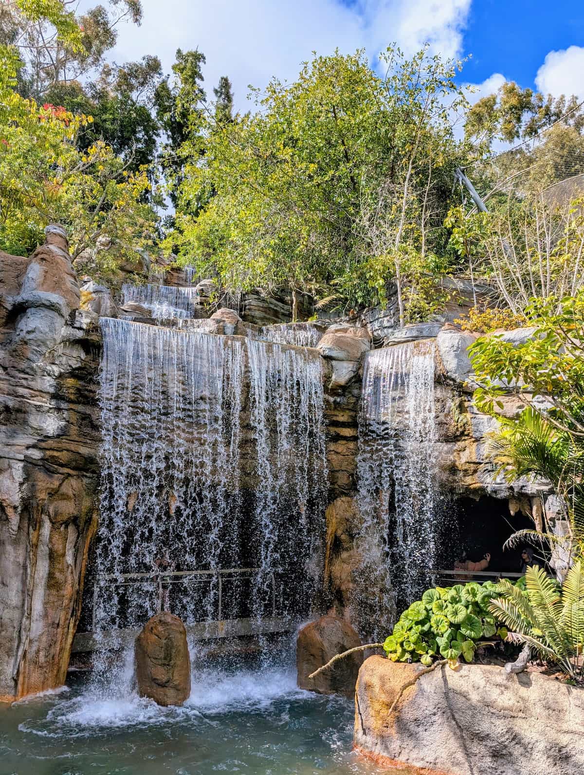 Large, multi-tier, man-made waterfall with a path behind the falls.