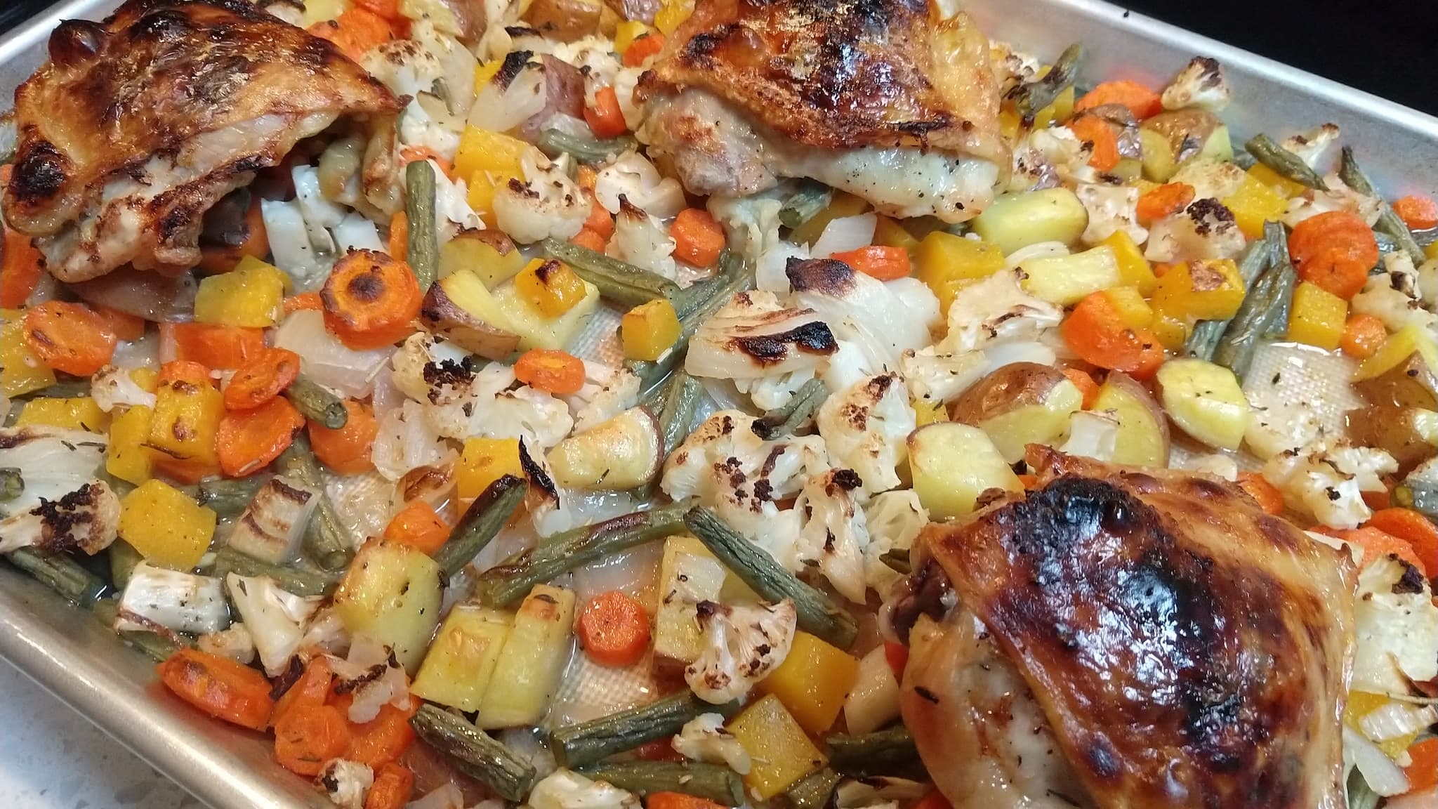 Chopped vegetables on a baking sheet with pieces of chicken on top