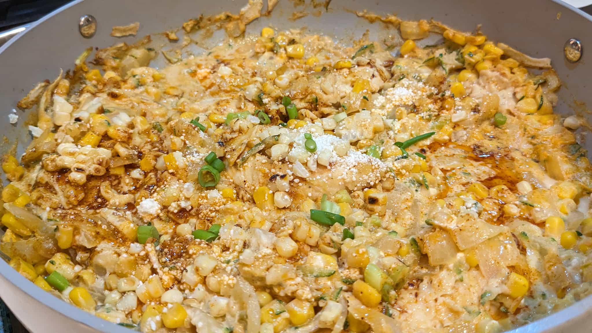 Large skillet with corn, onions, spices, and cheese over barely visible chicken tenders.