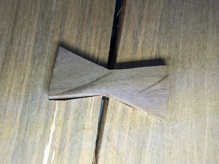 wooden bowtie cutout resting in a slot in unfinished wood across a crack