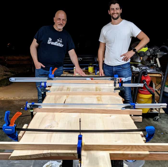 two men standing behind unfinished table clamped together