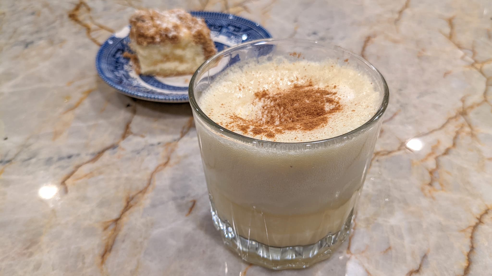 short glass with creamy drink and cinnamon next to coffee cake.