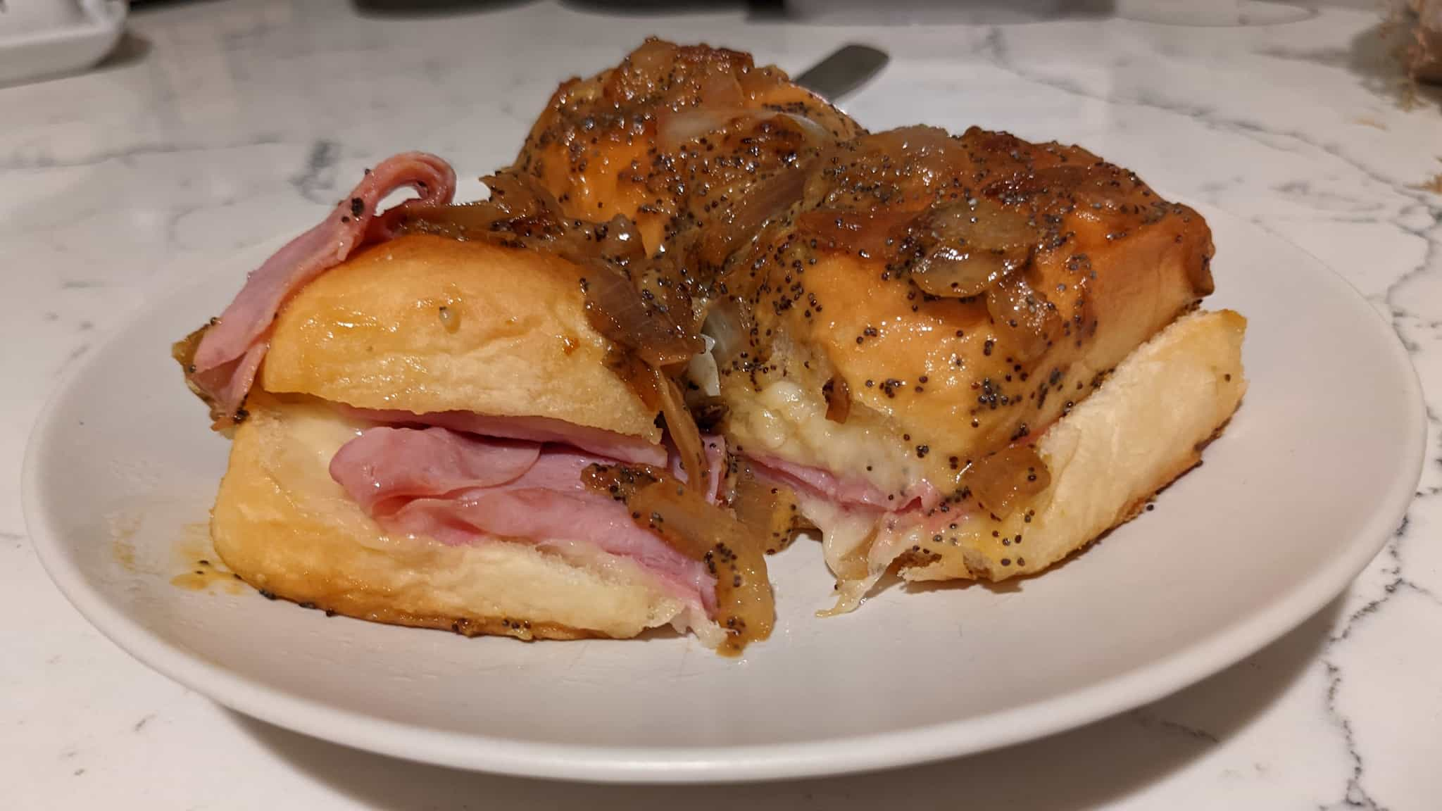 three ham and cheese sliders on a plate smothered with an onion poppy sauce