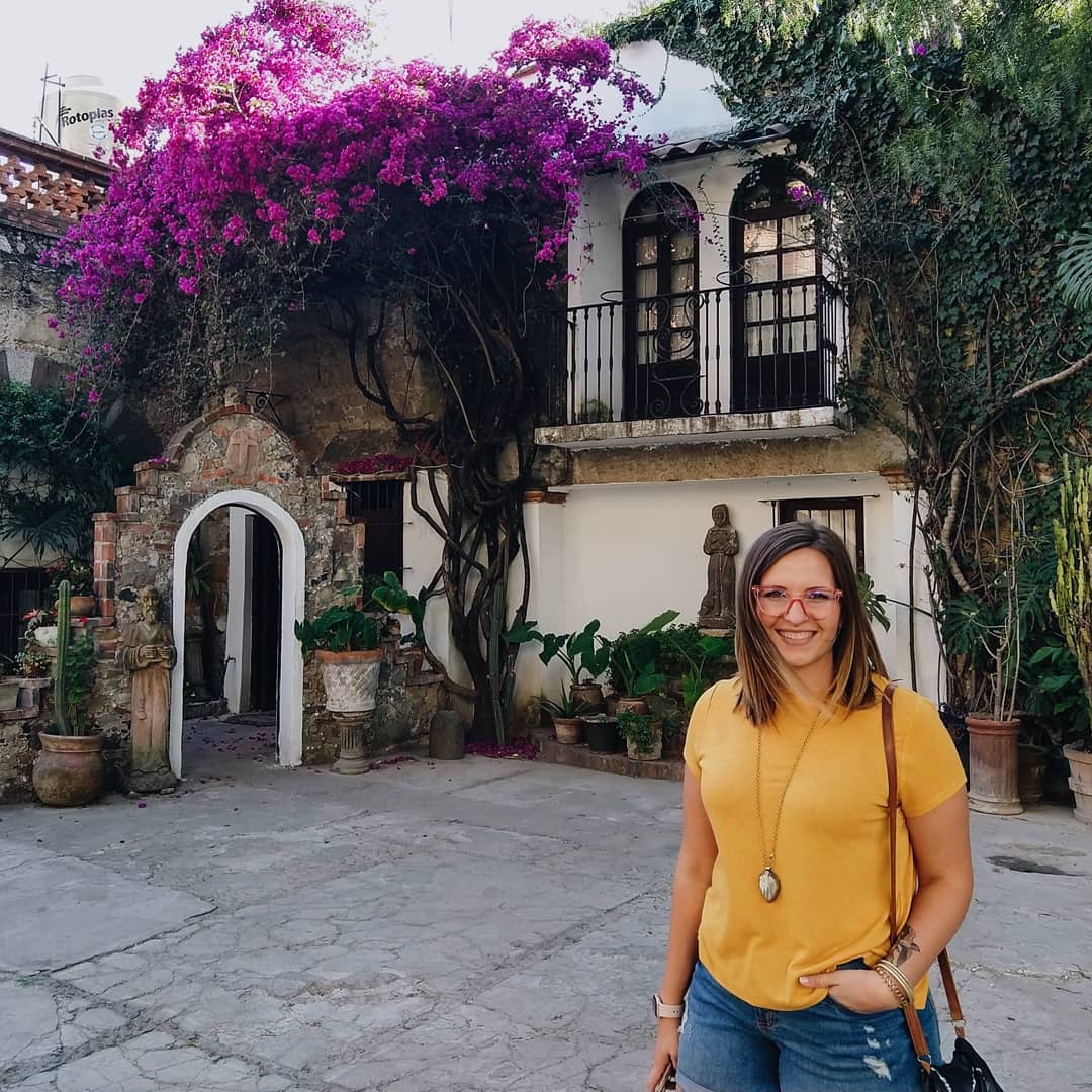 Woman standing in front of apartment with an arch, a large flowering bougainvillea vine, and other tropical plants