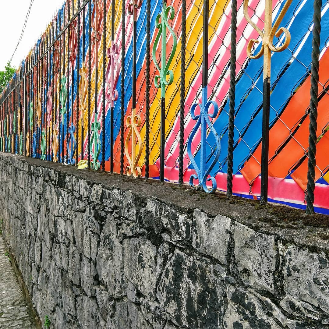 Stone wall topped with a colorful fence.