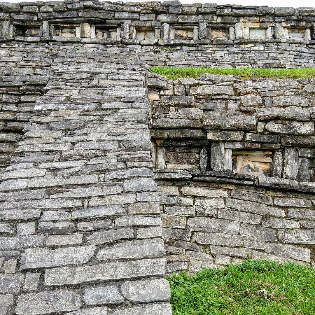 Multiple layers of a stone wall. Long and narrow stones are stacked upon each other. A row of stones is arranged into rectangular windows by standing some stones vertically.