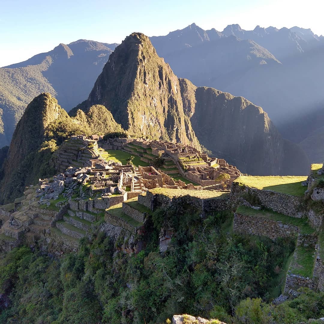 Sunlight shining onto the ruins of Machu Picchu as seen from a distance.