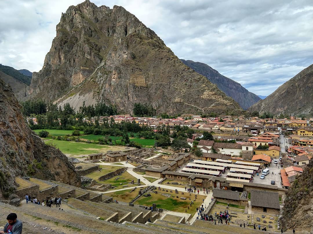 View looking down at a small town surrounded by tall mountains and ancient ruins.
