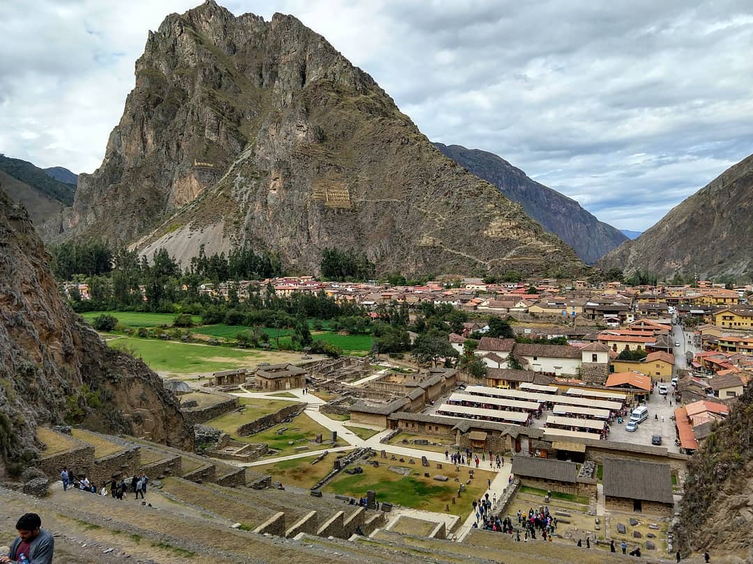 View looking down at a small town surrounded by tall mountains and ancient ruins.