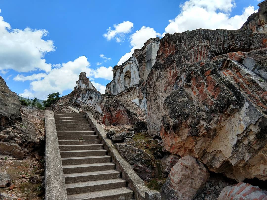 Large chunks of brick wall sit on the ground inside the foundation of a building next to a concrete staircase.