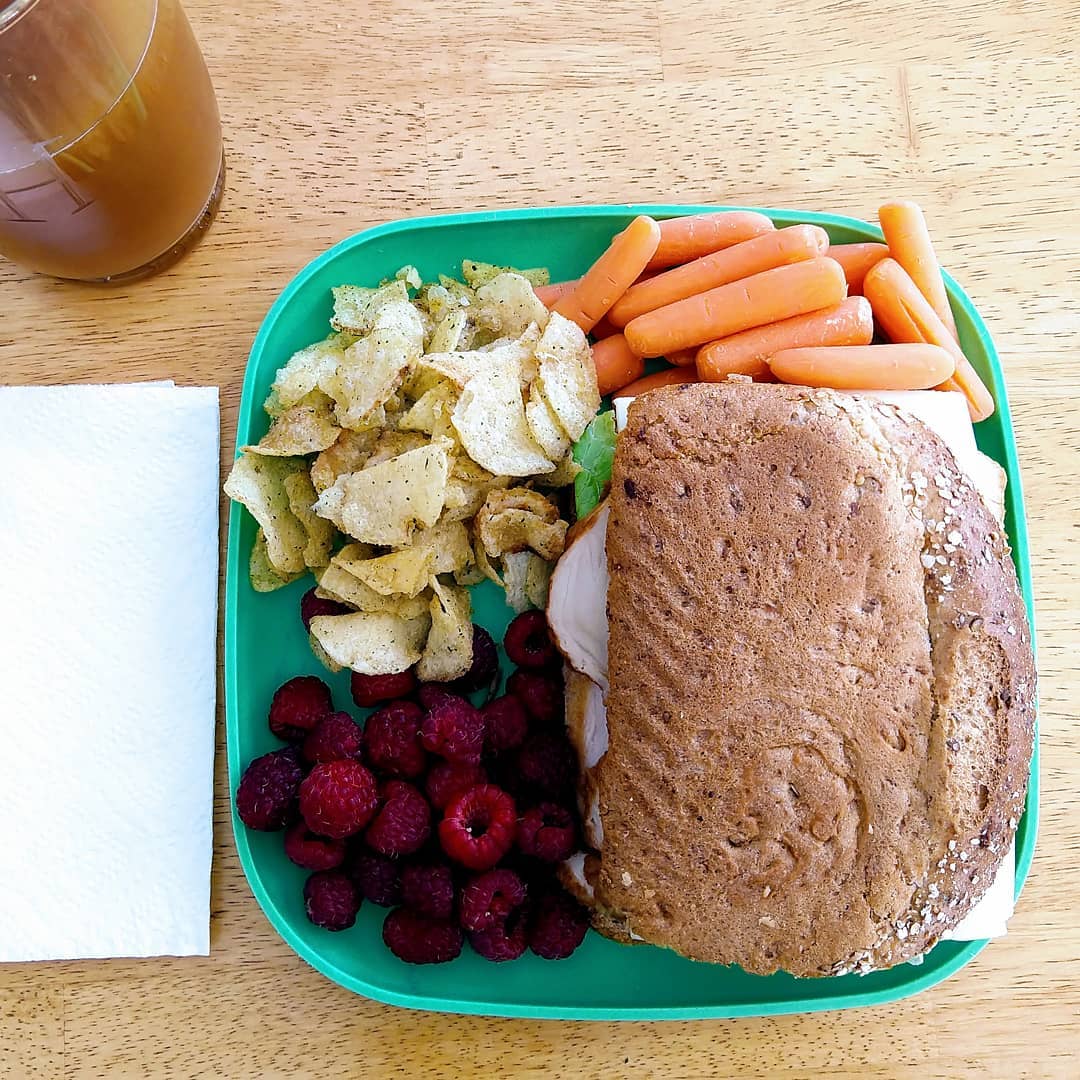 Plate with raspberries, baby carrots, chips, and a sandwich on a wood table.