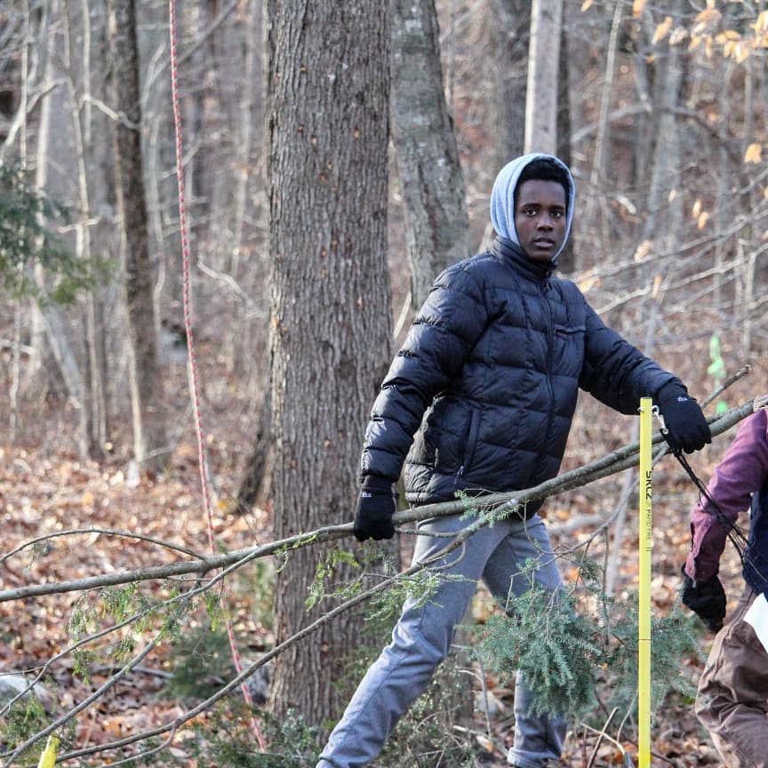 Teenager in a coat looks at the camera while carrying a branch.