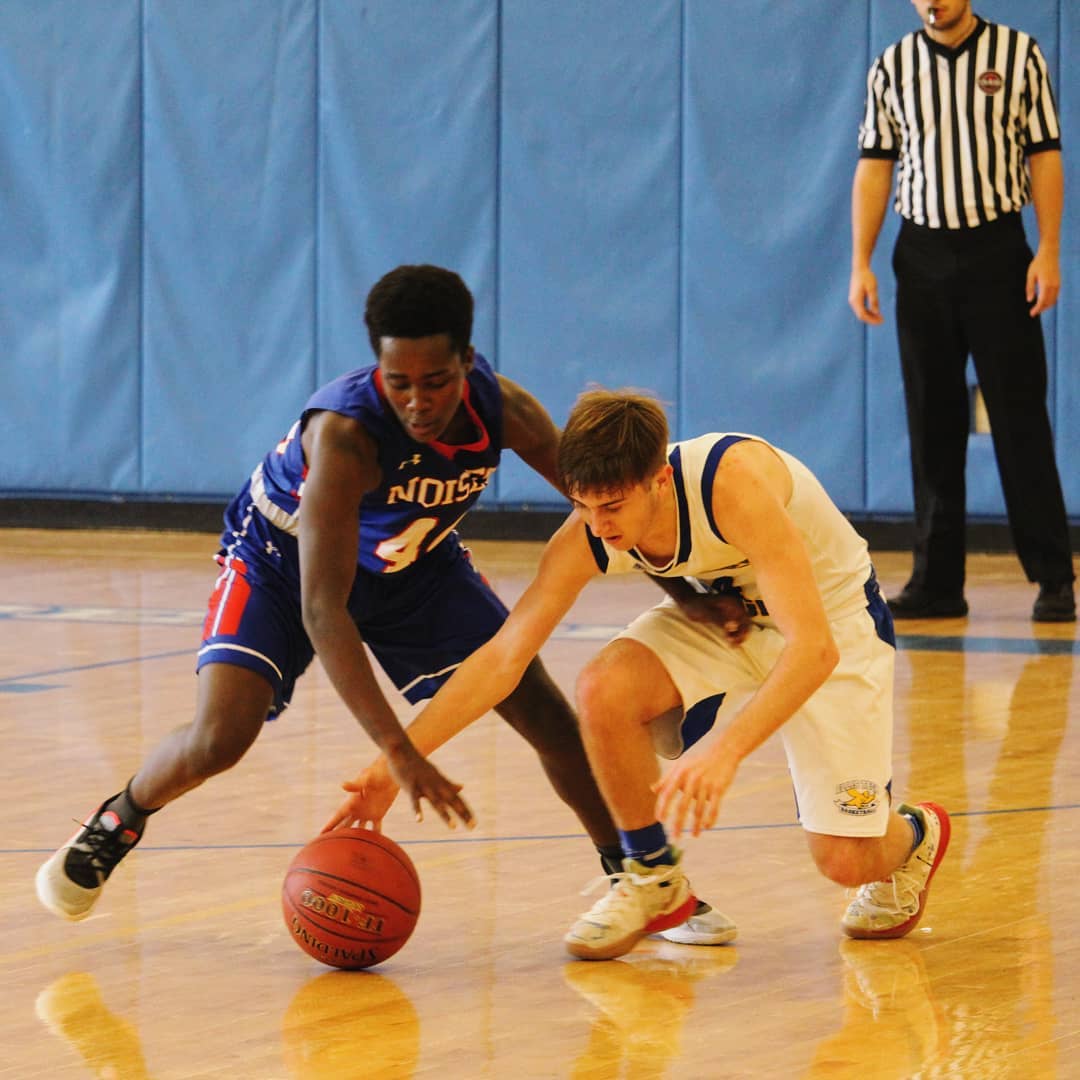 Boy in a 'Noises' basketball jersey stealing the ball from the opposing player.