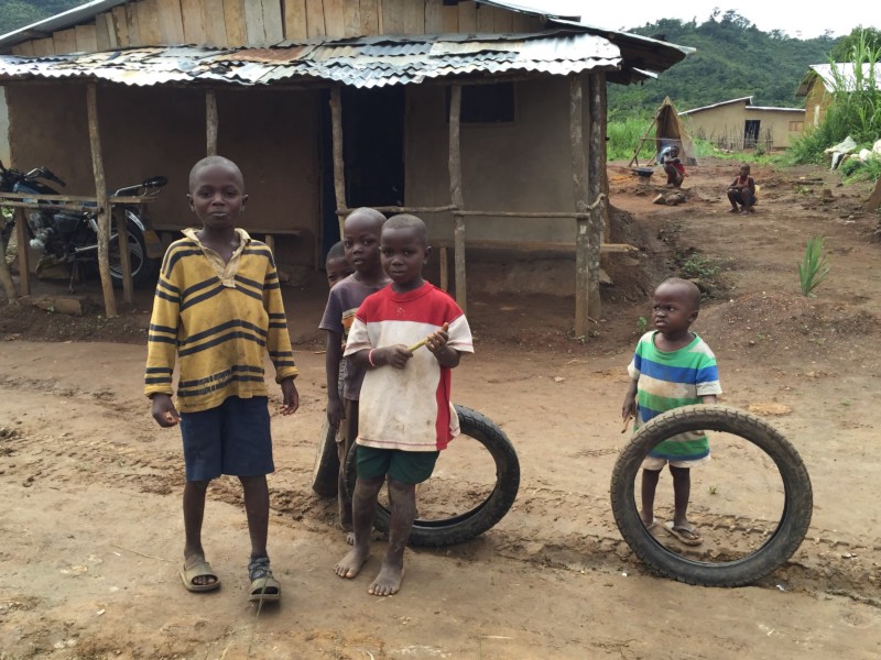 african children of different ages on a dirt road in front of a house with two motorcycle tires for games