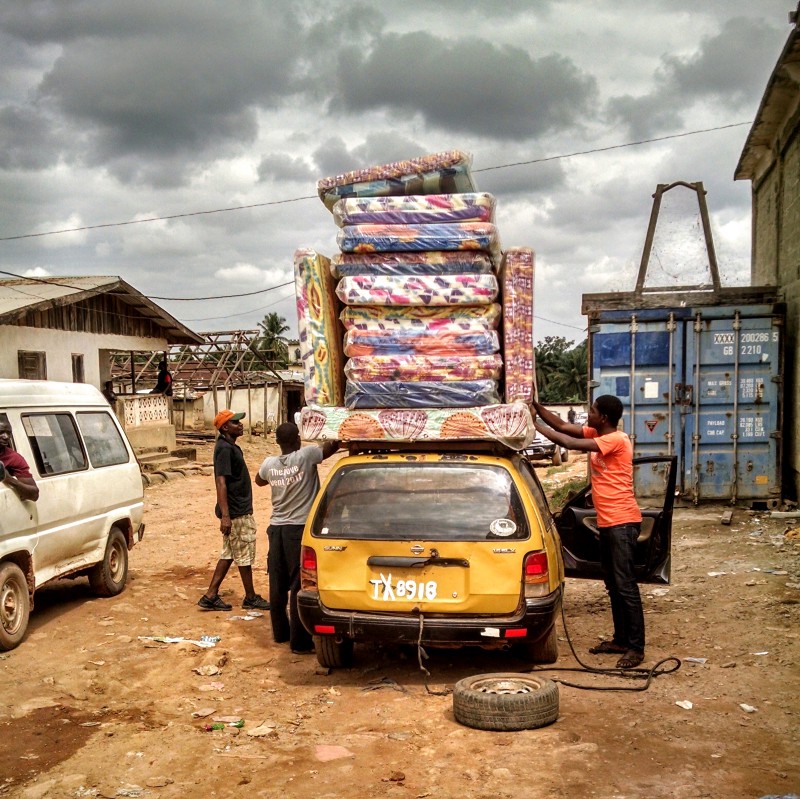 short yellow car with 3 men strapping about 15 mattresses to the top of the car