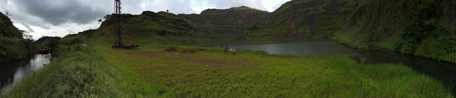 green hils enclosing a small lake with people walking a ways away