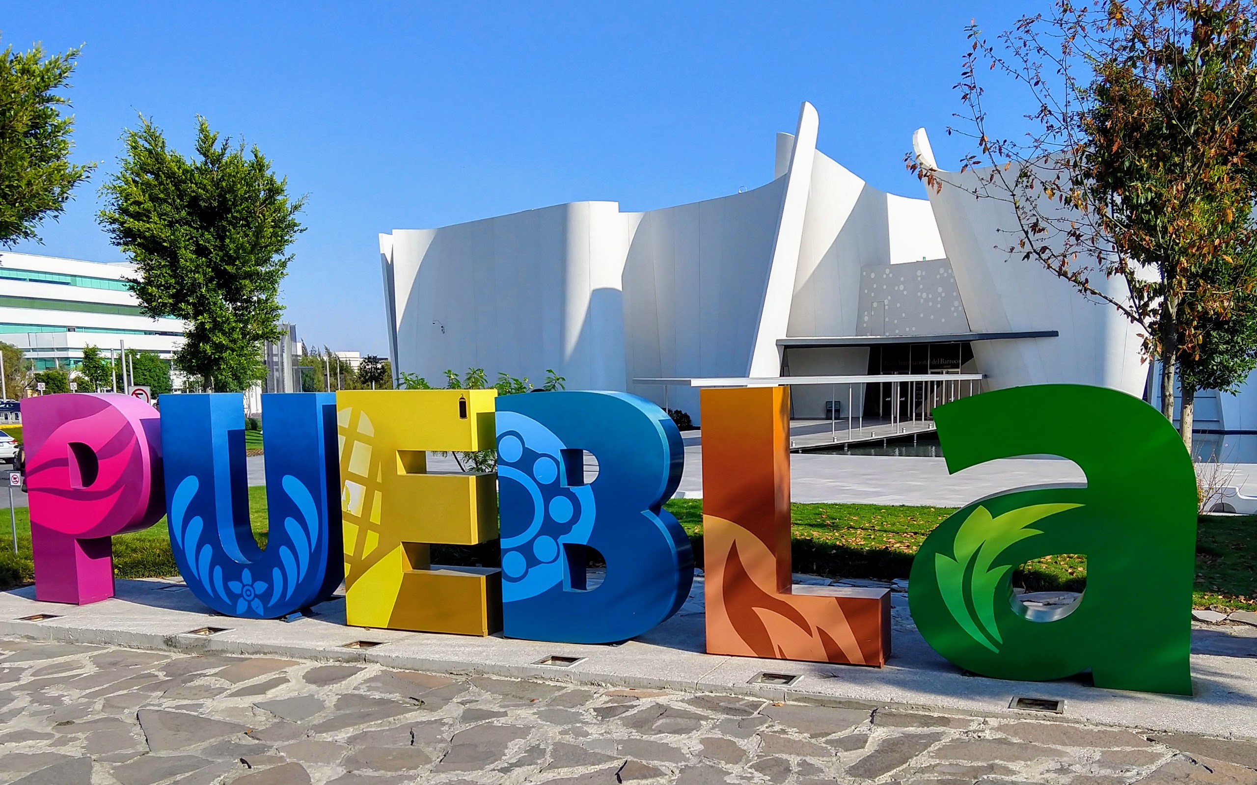 Colorful letters mounted to the ground spelling puebla with a white museum in the background with tall, white, curving walls