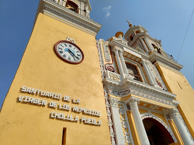 looking up at an ornately decorated yellow chapel with a sign reading santuario de la virgen de los remedios cholula puebla