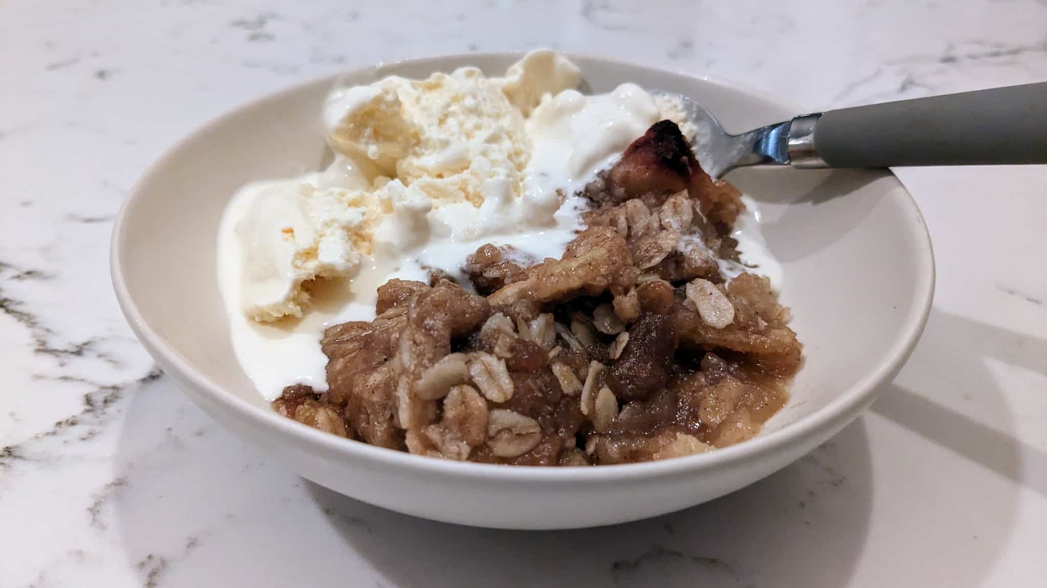 Bowl of oats and apples topped with vanilla ice cream.