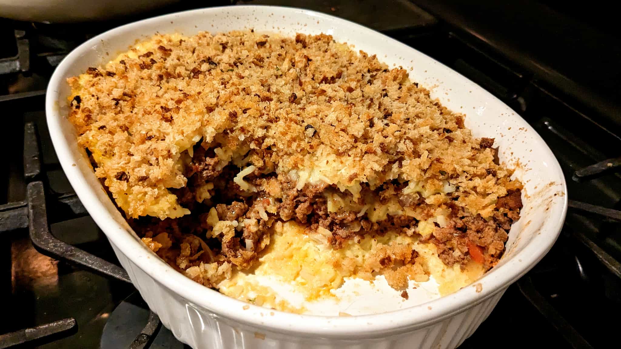 Casserole dish with some food removed showing layers of rice and ground beef topped with breadcrumbs.