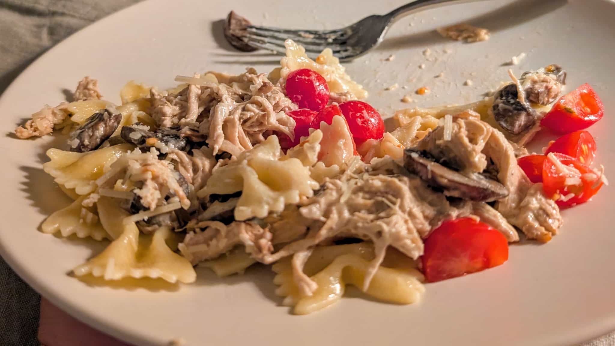 A plate with bowtie pasta. shredded chicken, mushrooms, and grape tomatoes.