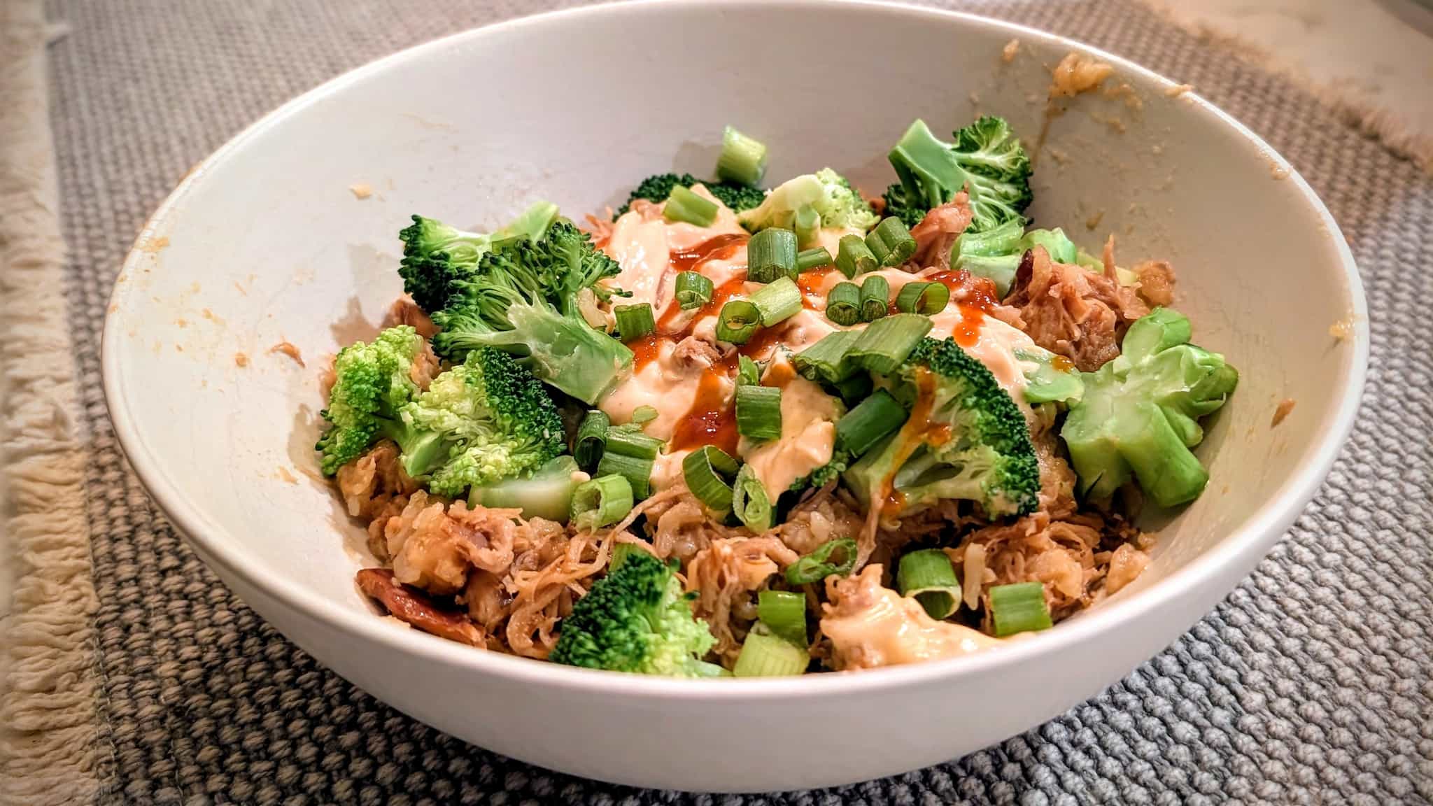 Bowl with rice and shredded chicken, covered in broccoli, green onions, and sauce.