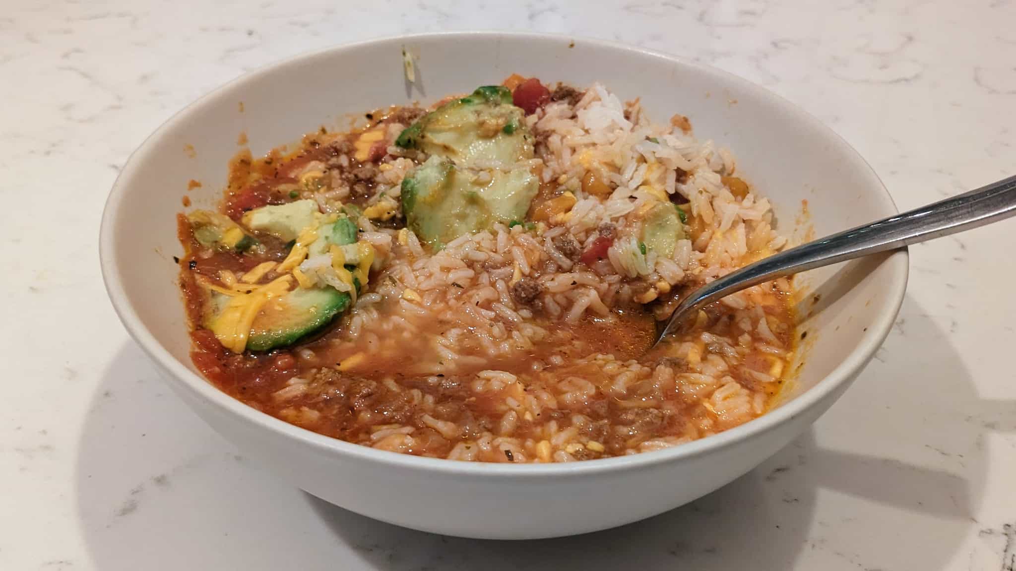 Bowl of rice, avocado slices, in a red soup.