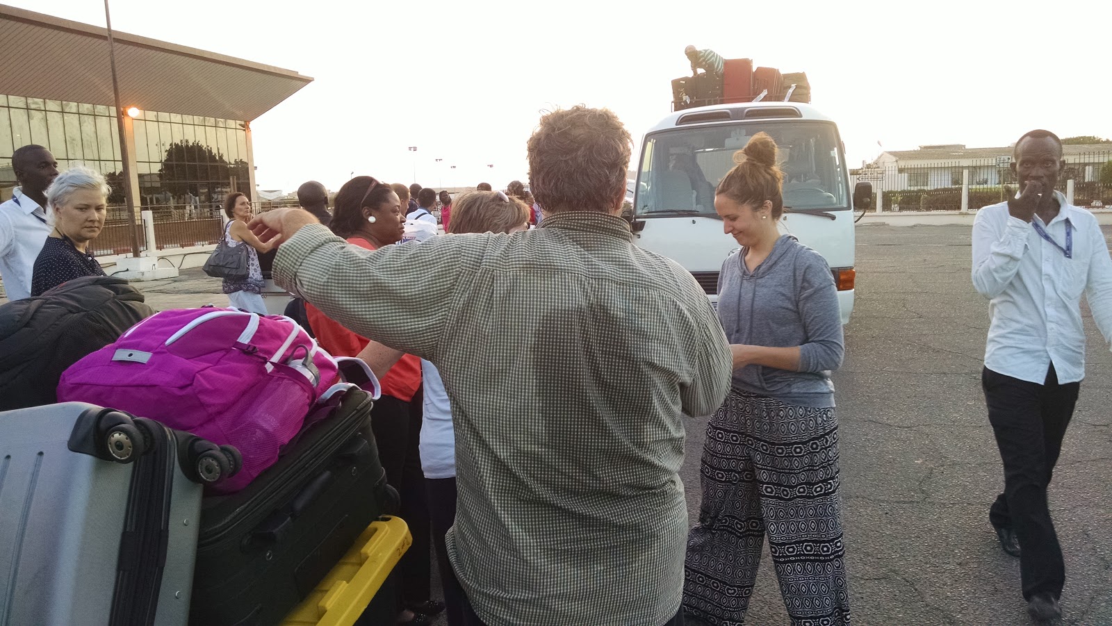 Crowd of people in a parking lot with lots of luggage with a white bus
